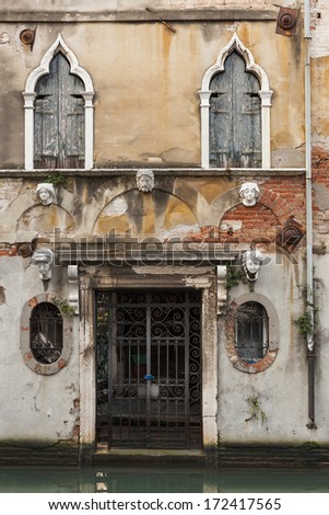 Old building facade with the entrance and sculptural faces in Venice, Italy.