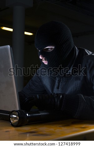 masked hacker sitting behind computer