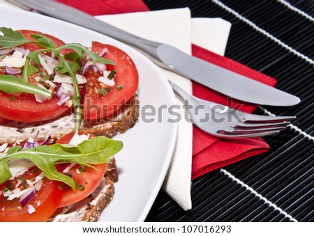 Fresh made tomato bread with onion, cream cheese, rocket salad and Parmesan cheese on a black tablecloth with cutlery