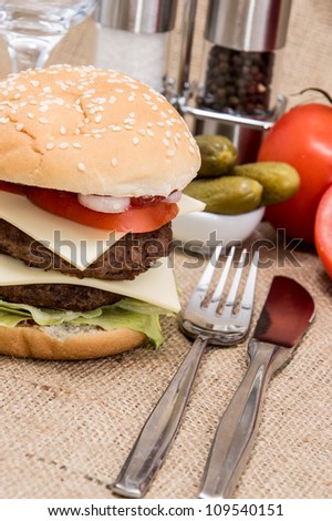 Double Burger with ingredients and cutlery on rustic background
