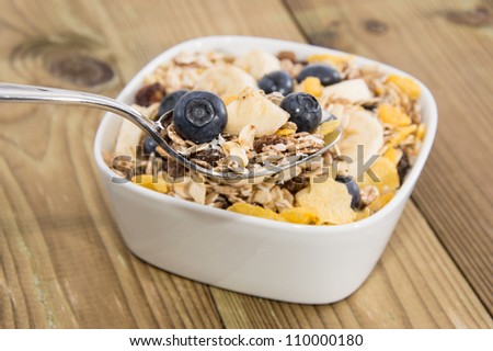 Muesli on a spoon with bowl in the background on wood