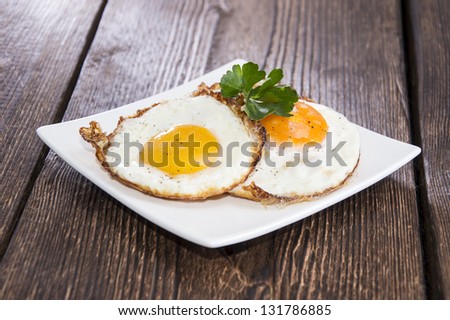 Fried Eggs on a plate (wooden background)