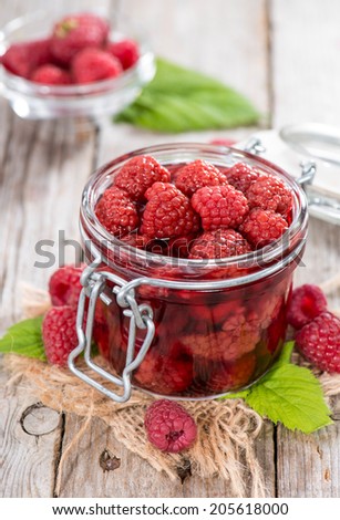 Glass with a portion of canned raspberries with some fresh fruits on wooden background