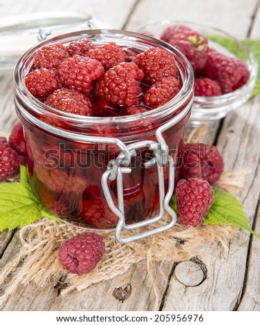 Glass with a portion of canned raspberries with some fresh fruits on wooden background