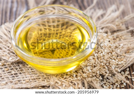 Sesame Oil with some Sesame Seeds on dark wooden table (close-up shot)