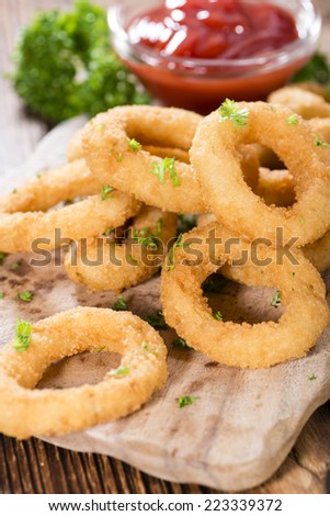 Portion of Onion Rings (homemade) with fresh herbs on  an old wooden table