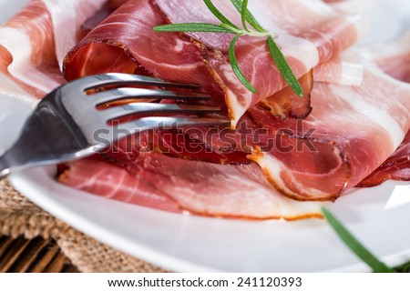 Portion of sliced smoked Ham with fresh herbs on wooden background