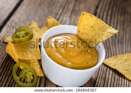 Nachos with Cheese Dip (close-up shot) on an wooden table