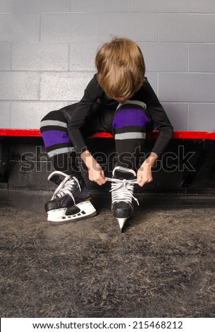A Young Boy Ties His Hockey Skates in Rink Dressing Room