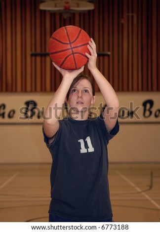 A young woman shoots a basketball in a gym.