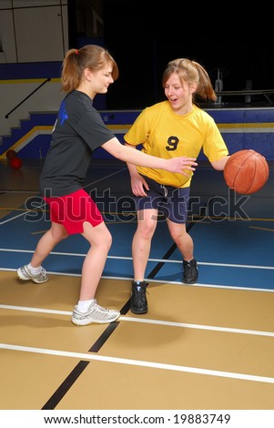 Two female basketball players scrimmage in school gym.