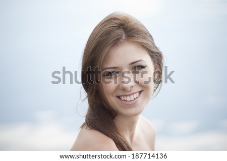 Young woman with wide smile looks at you. Reflection of the sky on background