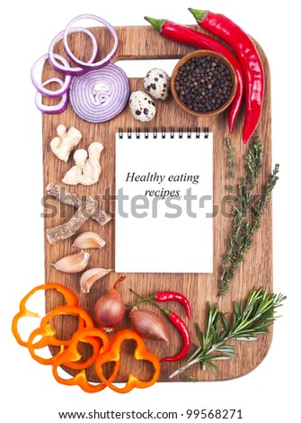 Open notebook and fresh vegetables on an old wooden cutting board. Isolated on white