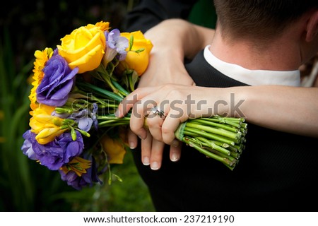 Bride holding bouquet of flowers around Groom\'s neck.
