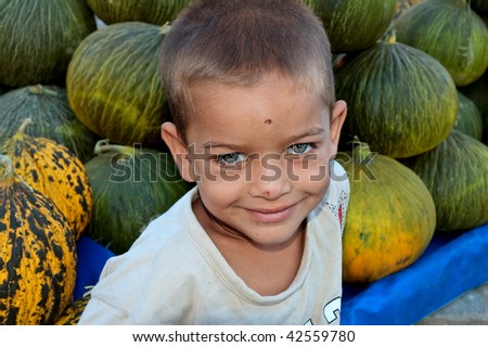 A very cute boy with beautiful blue eyes in front of melons his father grows and sells
