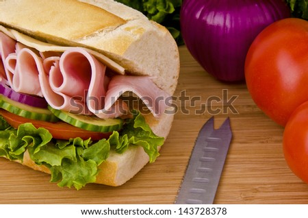 Sub sandwich on a cutting board. Tomatoes, onion and lettuce background.