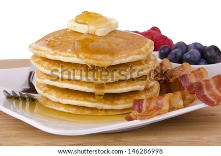 Stack of pancakes and bacon with fruits on background. Front view.