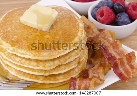 Stack of pancakes and bacon with fruits on background. Top view.