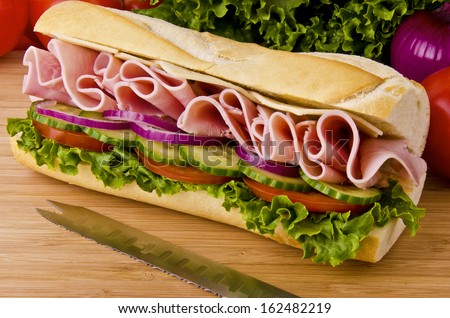 Sub sandwich on a cutting board. Tomatoes, onion and lettuce background.