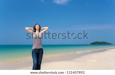Pretty young woman with arms raised and eyes shut standing on the tropical beach relaxed. Expressing positivity