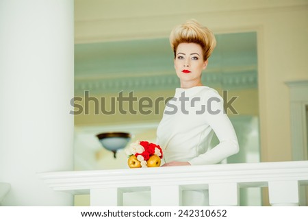Beautiful young bride in white and red dress with a bouquet of standing at the stairs