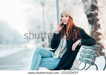 young woman in winter park talking mobile phone, sitting on the bench