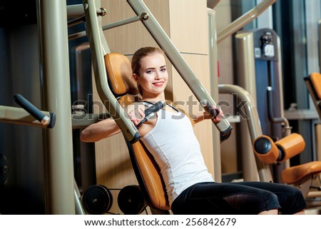 sport, fitness, lifestyle and people concept - young woman flexing muscles on gym machine.