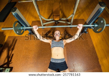 young woman doing exercises with barbell on bench in the gym. Bar Bench Press.
