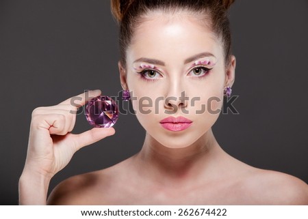 Young beautiful woman with perfect makeup, drawing bows, admiring the gem.