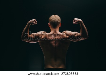 a muscular young man showing his biceps isolated on black background