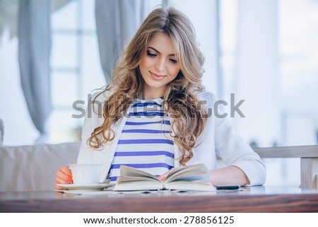 beautiful young girl in outdoor cafe reading a book and drinking coffee. phone. student. business woman