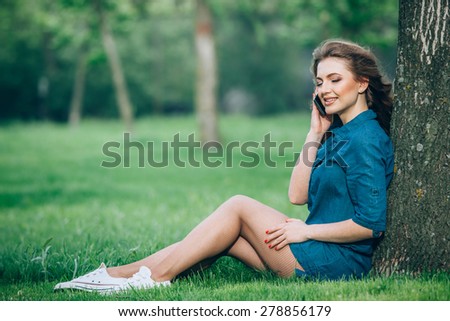 Pretty young caucasian woman  sitting outside under a tree talking on a smartphone device. Filtered effects