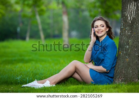 Pretty young caucasian woman  sitting outside under a tree talking on a smartphone device. Filtered effects