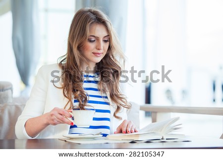 beautiful young girl in outdoor cafe reading a book and drinking coffee. phone. student. business woman