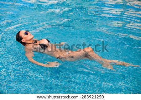 Sexy swimmer. A slender sexy lady in bikini balancing on her back in blue water.