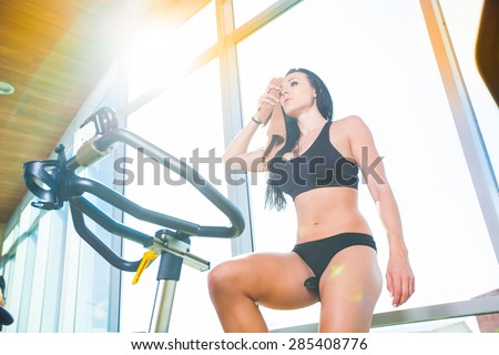 Beautiful woman at the gym on bike, cycle, sunny gym, general plan, weary