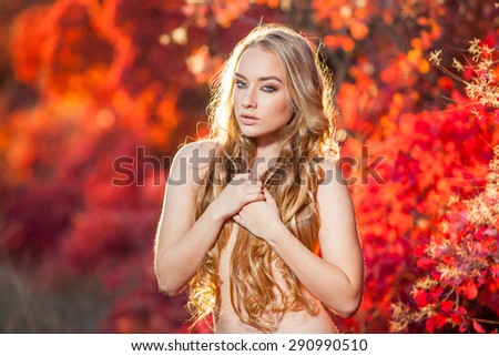 young woman on a background of red and yellow autumn leaves with beautiful curly hair on his chest, with no clothes
