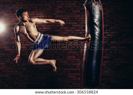 muscular handsome fighter giving a forceful forward kick during a practise round with a boxing bag, kickboxing.