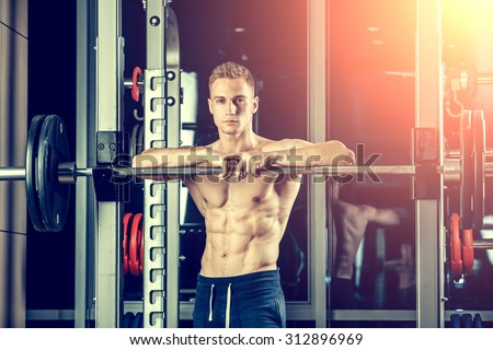 Closeup portrait of a muscular man workout with barbell at gym. Brutal bodybuilder athletic man with six pack, perfect abs, shoulders, biceps, triceps and chest