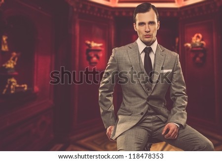 Confident man in classic grey suit sitting on chair in cabinet