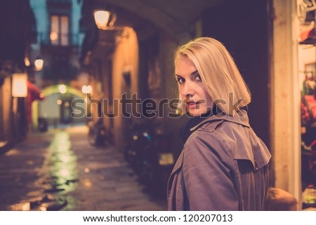 Beautiful blond woman in raincoat walking alone outdoors at night