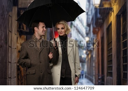 Elegant couple with umbrella walking outdoors in the rain