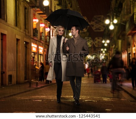 Elegant couple with umbrella outdoors on rainy evening