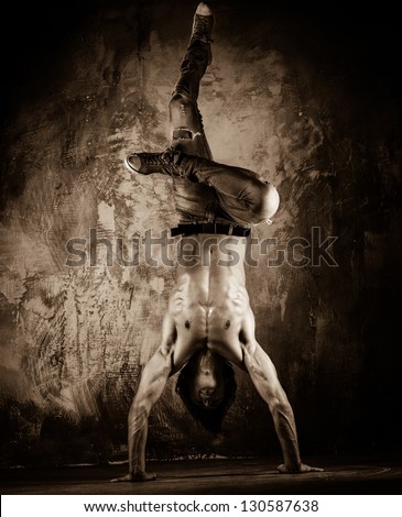 Toned picture of young man with naked torso doing acrobatic movements