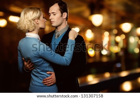Man in jacket embracing woman in blue cardigan outdoors at night