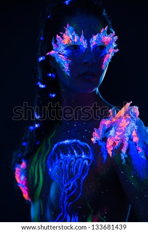 Beautiful woman with body art glowing in ultraviolet light