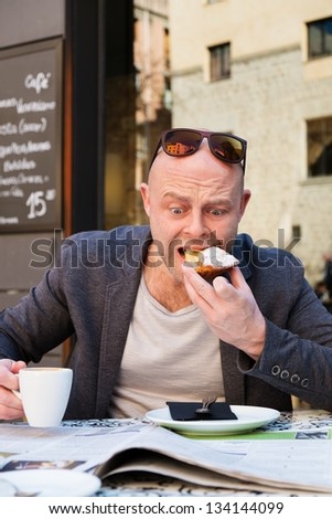 Surprised middle-aged man reading newspaper behind table in street cafe during coffee pause