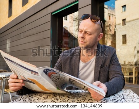 MIddle-aged man reading newspaper behind table in street cafe