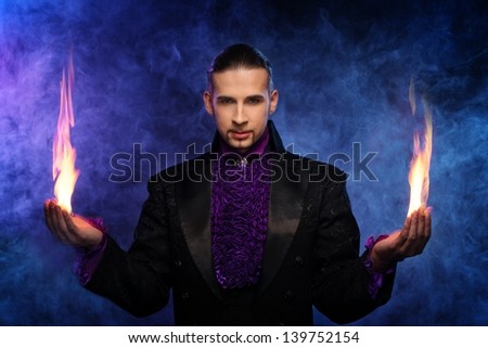 Young brunette magician in stage costume performing flame tricks