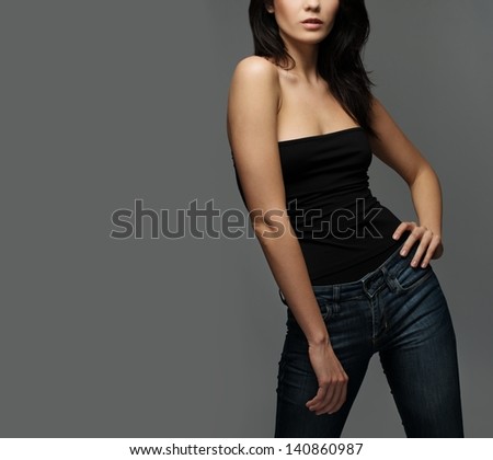 Young brunette woman in jeans and black top isolated on grey background